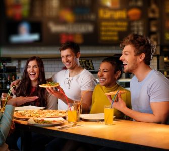 Cheerful multiracial friends having fun eating in pizzeria.