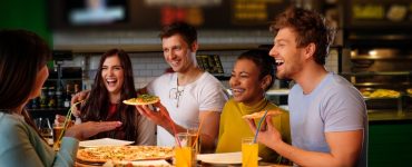 Cheerful multiracial friends having fun eating in pizzeria.
