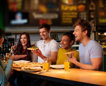 Cheerful multiracial friends having fun eating in pizzeria.
