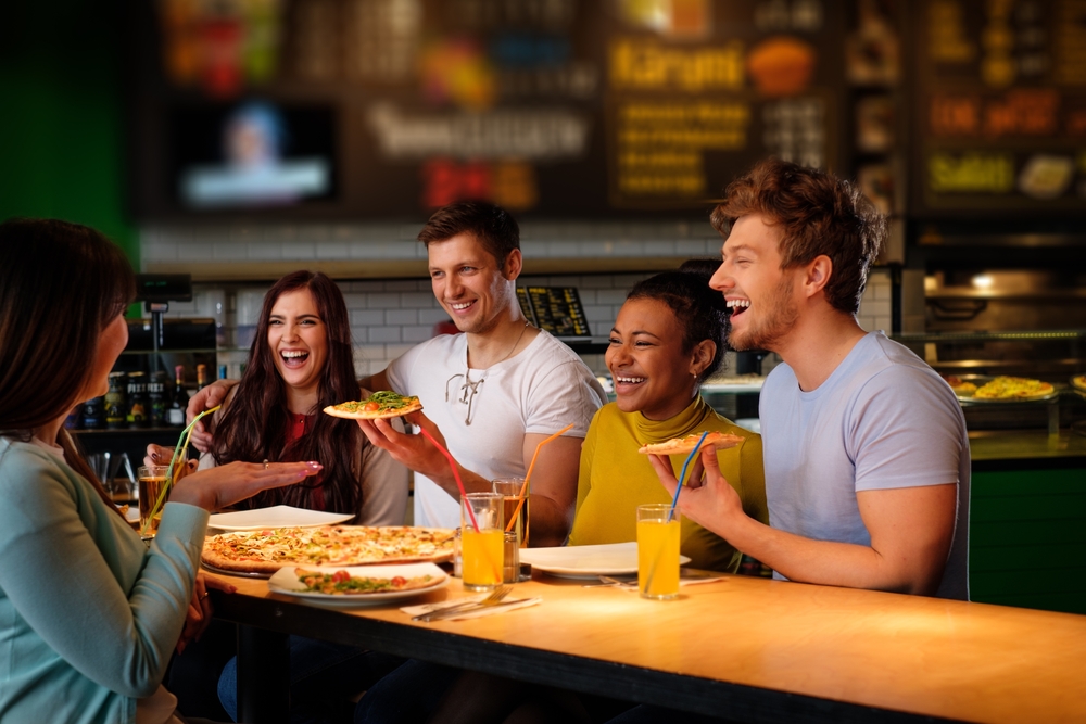 Cheerful multiracial friends having fun eating in pizzeria.