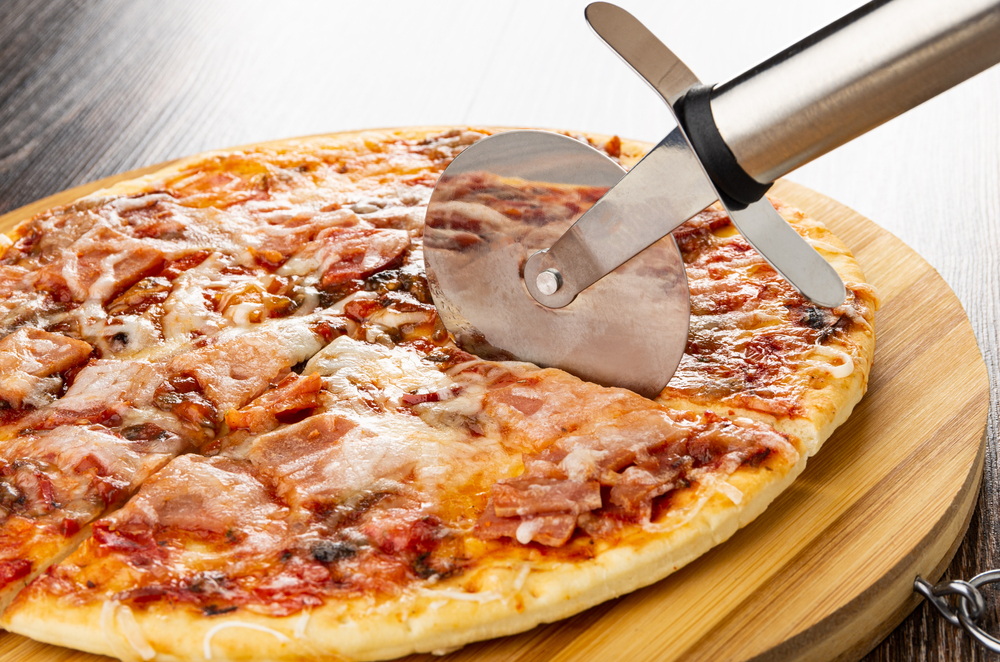 Cutting pizza with pizza cutter on striped bamboo cutting board